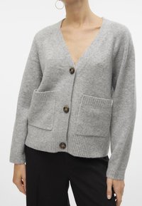 Gray wool cardigan featuring a deep V-neck, front pockets, and ribbed hem. It has three large, round buttons in a contrasting material.