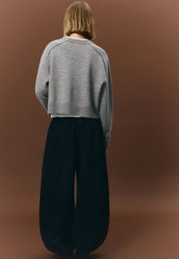 Pulover gri scurt cu gât rotund, asortat cu pantaloni negri cu croială largă. Finisaj tricotat texturat. Design simplu, fără modele sau accente vizibile.