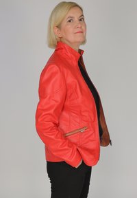 Röd läderjacka med hög krage och dragkedja fram. Har sidofickor och kontrasterande brun foder, mjuk textur.