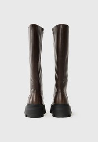 Stivali alti fino al ginocchio in pelle marrone con un design elegante, cerniere laterali e suole in gomma nera spessa per stabilità e trazione.