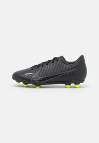 Botín de fútbol Nike Mercurial negro con tacos amarillos, diseño con cordones y patrón texturizado a rayas sobre un fondo blanco.