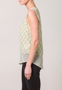 Top senza maniche di colore verde chiaro con motivi geometrici, caratterizzato da un frontale trasparente e un orlo solido. Il design presenta una silhouette fluida e un retro arrotondato.