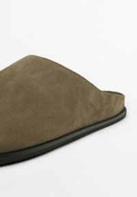 Mockasins i olivgrön mocka med en mjuk textur, låg profil och minimalistisk design. Har en rund tå och svart sula.