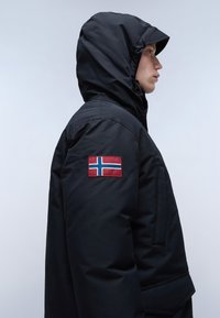 Svart isolerad jacka med huva, med en norsk flagga på vänster ärm. Slät textur, slitstarkt material och en figurnära design.