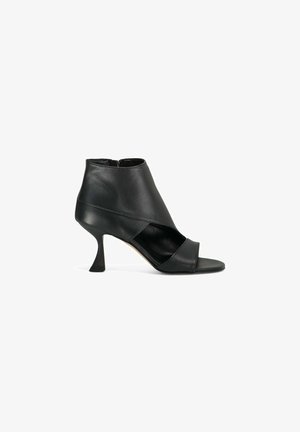Bottine en cuir noir à bout ouvert, fermeture éclair latérale et talon mi-hauteur à forme unique.