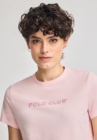 Rosa bomullströja med rund hals, med broderad text "POLO CLUB" och "ETABLERAD 2012" i kontrasterande färger. Slät textur.