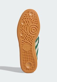 Sole of green Adidas sneaker showing gum rubber outsole with circular and grid tread patterns and Adidas logo near heel.