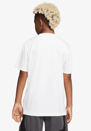 Giovane con capelli biondi ricci visto da dietro, che indossa una maglietta bianca a maniche corte semplice e pantaloncini sportivi grigi.