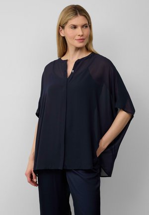 Blouse légère bleu marine avec des manches dolman courtes, un placket boutonné et une coupe décontractée, fabriquée en tissu transparent avec une texture lisse.