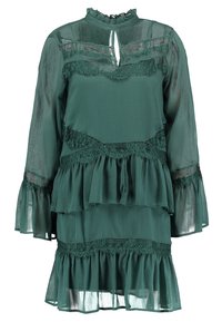 Teal lager klänning i genomskinligt tyg med volangärmar, spetsdetaljer, hög halsringning och en nyckelhålsdetalj fram.