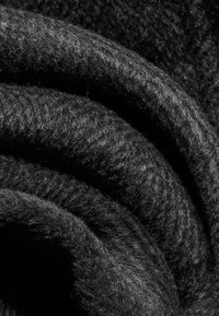 Tissu en laine noir doux et épais avec des fibres visibles, étroitement plié en courbes superposées créant de profonds ombres et reflets.