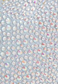 Tissu à paillettes présentant de nombreuses gemmes circulaires iridescentes de tailles variées. La surface est texturée et reflète la lumière dans plusieurs couleurs.