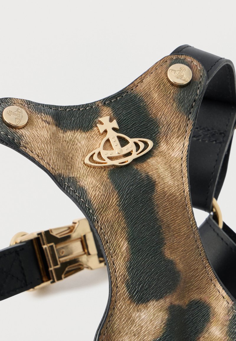 Tarnfarbenes Lederharness mit goldfarbenen Metallbeschlägen, versehen mit einem Logodetail und schwarzen Riemenakzenten. Strukturierte Oberfläche und elegantes Design.