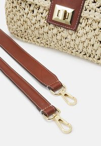 Torebka z plecionki słomkowej z brązowym skórzanym paskiem i złotymi elementami. Posiada bezpieczne zapięcie i szczegółowe przeszycia na pasku.