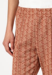 Mønstret tapered bukser i rust med et geometrisk design i krem. Har en elastisk livlinje og en glat stofftekstur.