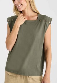 Haut sans manches vert olive en coton doux avec une encolure large. Présente des accents en métal doré sur les épaules, une coupe décontractée et une texture lisse.