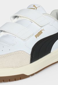 Λευκό αθλητικό παπούτσι Puma με μαύρη πλαϊνή ρίγα, μπεζ σουέντ μυτερό μέρος, χρυσό λογότυπο Puma και δύο λευκές λουρίδες με βέλκρο.