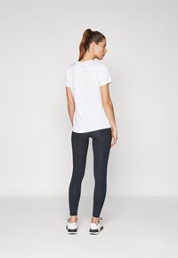 Maglietta sportiva corta bianca a maniche corte e leggings neri, abbinati a scarpe sportive bianche e nere, indossati in posizione eretta visto da dietro.