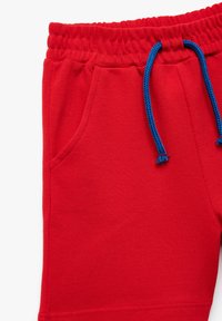 Röda texturerade shorts med elastisk midja och blå dragsko, med en sidficka på vänster ben.
