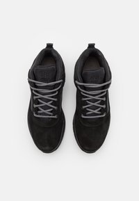 Paire de baskets en daim noir avec des lacets gris, une languette rembourrée et un col de cheville, vues de dessus sur un fond blanc.