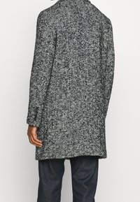 Cappotto con motivo pied de poule in bianco e nero, vestibilità sagomata, maniche lunghe e taglio a metà lunghezza, realizzato in tessuto misto lana strutturato.