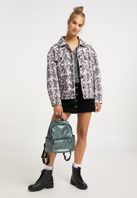 Giacca in denim con stampa houndstooth rosa e nera, abbinata a una gonna in corduroy nera. Gli accessori includono uno zaino metallico verde e stivaletti neri con lacci.