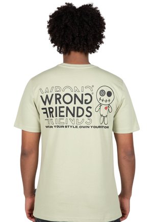 Light green t-shirt featuring a graphic with "WRONG FRIENDS" text and a cartoon character with stitched details, set against a plain background.