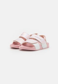 Vaaleanpunaiset ja valkoiset sandaalit, joissa on säädettävät hihnat, teksturoitu pinta ja litteä pohja, jossa on pehmustettu sisäpohja mukavuutta varten.