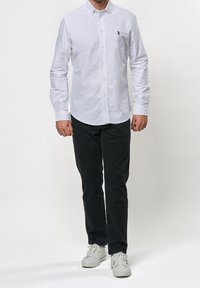 Camicia bianca a maniche lunghe con bottoni, con un piccolo logo sul petto. Abbinata a pantaloni neri e sneakers bianche.