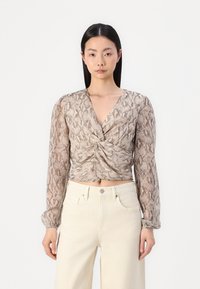 Blusa a maniche lunghe tagliata in tessuto leggero con stampa serpente, caratterizzata da un davanti torcigliato e una scollatura a V profonda. Abbinata a pantaloni di colore chiaro.