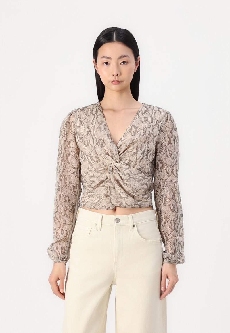 Blusa a maniche lunghe tagliata in tessuto leggero con stampa serpente, caratterizzata da un davanti torcigliato e una scollatura a V profonda. Abbinata a pantaloni di colore chiaro.