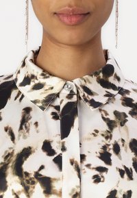 Blusa con colletto in stampa animale ad acquerello nei colori beige, nero e verde. Presenta un bottone decorativo con un accento di strass.