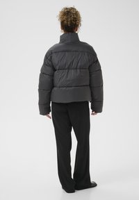 Kratka pufasta jakna u tamnosivoj boji, s visokim ovratnikom, horizontalnim kvadratnim uzorkom i oversized krojem, u kombinaciji s crnim širokim hlačama.