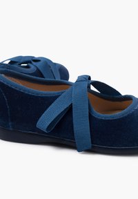 Bailarinas de terciopelo azul con puntera redondeada, cinta decorativa de cruce y un forro interior suave. Suelas de goma para mayor agarre.