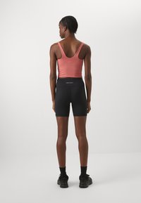 Pantaloni sportivi neri abbinati a una canotta rosa, con design a schiena scoperta e tessuto morbido. I pantaloni hanno una vita alta e sono privi di fantasie.