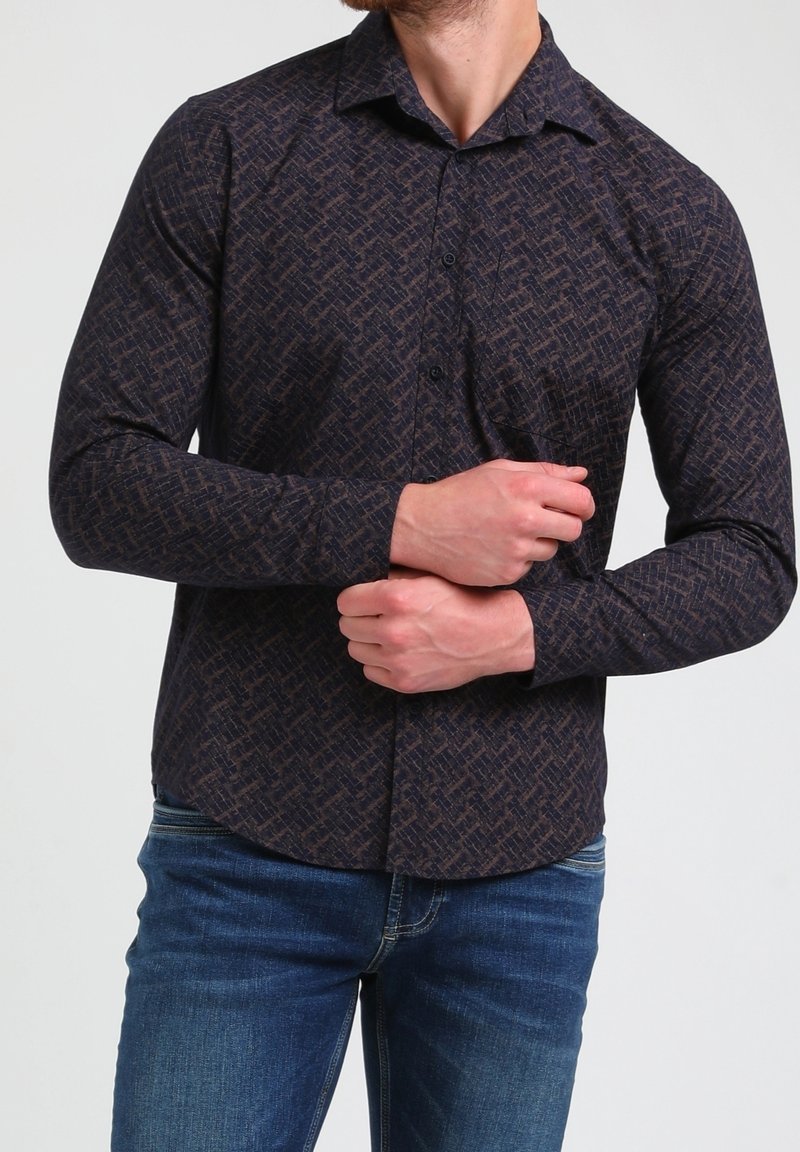 Camicia a maniche lunghe, di colore blu navy, con bottoni e un motivo geometrico testurizzato in marrone scuro. Presenta un colletto e un orlo arrotondato. Indossata con jeans blu.