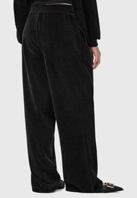 Svarta sammetbyxor med en lös passform, utrustade med elastisk midja och sidofickor. Tyget verkar mjukt och glättigt.