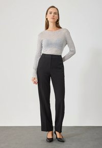 Grijs top met lange mouwen gecombineerd met zwarte, op maat gemaakte broek. De outfit heeft een aansluitende pasvorm, een gladde textuur en strakke zwarte hakken.