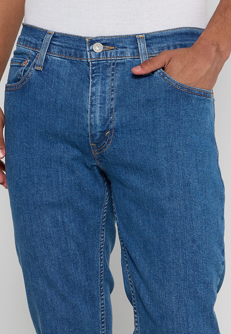 Jeans in denim blu scuro con design a gamba dritta, tasche anteriori e chiusura con bottone. Presentano cuciture visibili e una texture liscia.