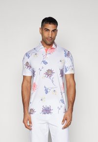 Kortermet polo skjorte i hvit med fargerike blomster mønstre i blå, rosa og gul; har en klassisk krage og tre-knapps placket.