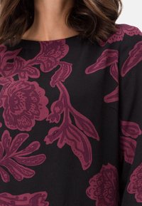 Tela negra con grandes patrones florales en burdeos. Presenta un escote redondo y mangas largas, mostrando una superficie suave y ligeramente texturizada.