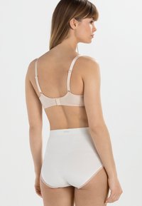 Sostenedor beige con tirantes ajustables y cierre de gancho, combinado con bragas blancas de talle alto que presentan un ribete de encaje en los bordes.
