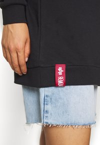 Sweat-shirt noir avec ourlet côtelé et étiquette rouge. Associé à un short en jean bleu clair déchiré avec bords effilochés.