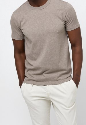 T-shirt marron à manches courtes en coton, avec un col rond et une texture lisse, associé à un pantalon de couleur claire.