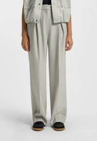 Ljusgrå vida byxor tillverkade av textil med struktur, med framfållar, hög midja och avslappnad passform. Kombineras med svarta sneakers.