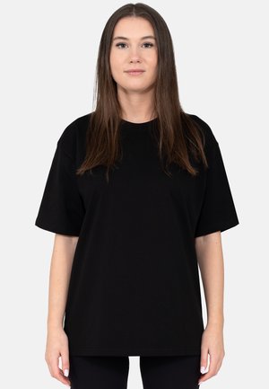 Schwarzes Baumwoll-T-Shirt mit kurzen Ärmeln, rundem Ausschnitt, legerer Passform und glatter Textur, getragen mit schwarzen Leggings. Schlichtes Design, keine Muster.