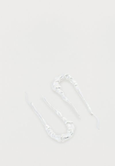 Boucles d'oreilles en argent présentant un design torsadé et allongé avec une finition brillante et des irrégularités subtiles dans la texture.