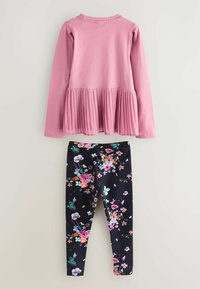 Lyserød langærmet bluse med plisseret kant og sorte leggings med et farverigt blomsterprint, herunder sommerfugle og fugle.