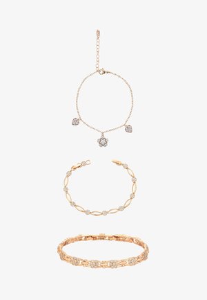 Trois bracelets en or avec des accents de pierres précieuses transparentes ; le supérieur a des breloques en forme de cœur et de fleur, le milieu a des maillons ovales et ronds, le bas présente un motif de grappe florale.