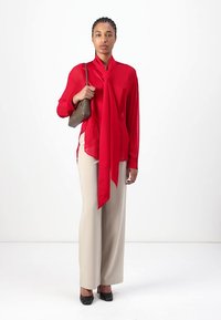 Rød bluse med scarf-detalj, kombinert med lysebeige vide bukser og sorte hæler. Glatt stoff og skreddersydd passform.